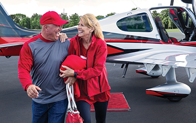 A man and a woman smiling while walking away from a cirrus aircraft